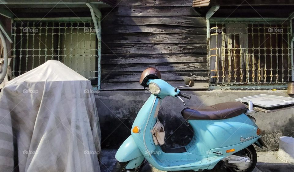 A water blue motorcycle parked outside a wooden house