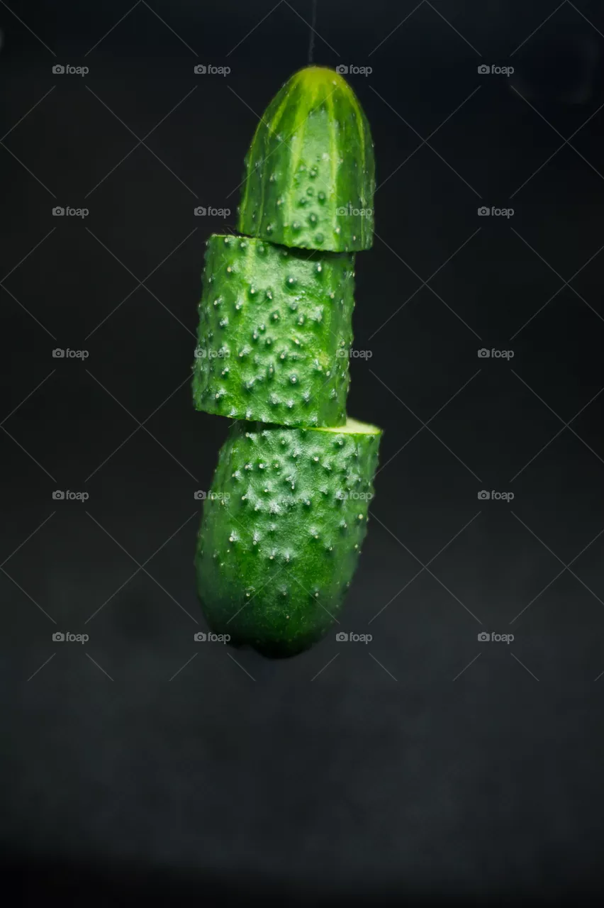 Close-up of a cucumber cut into three parts in the air on a black background.