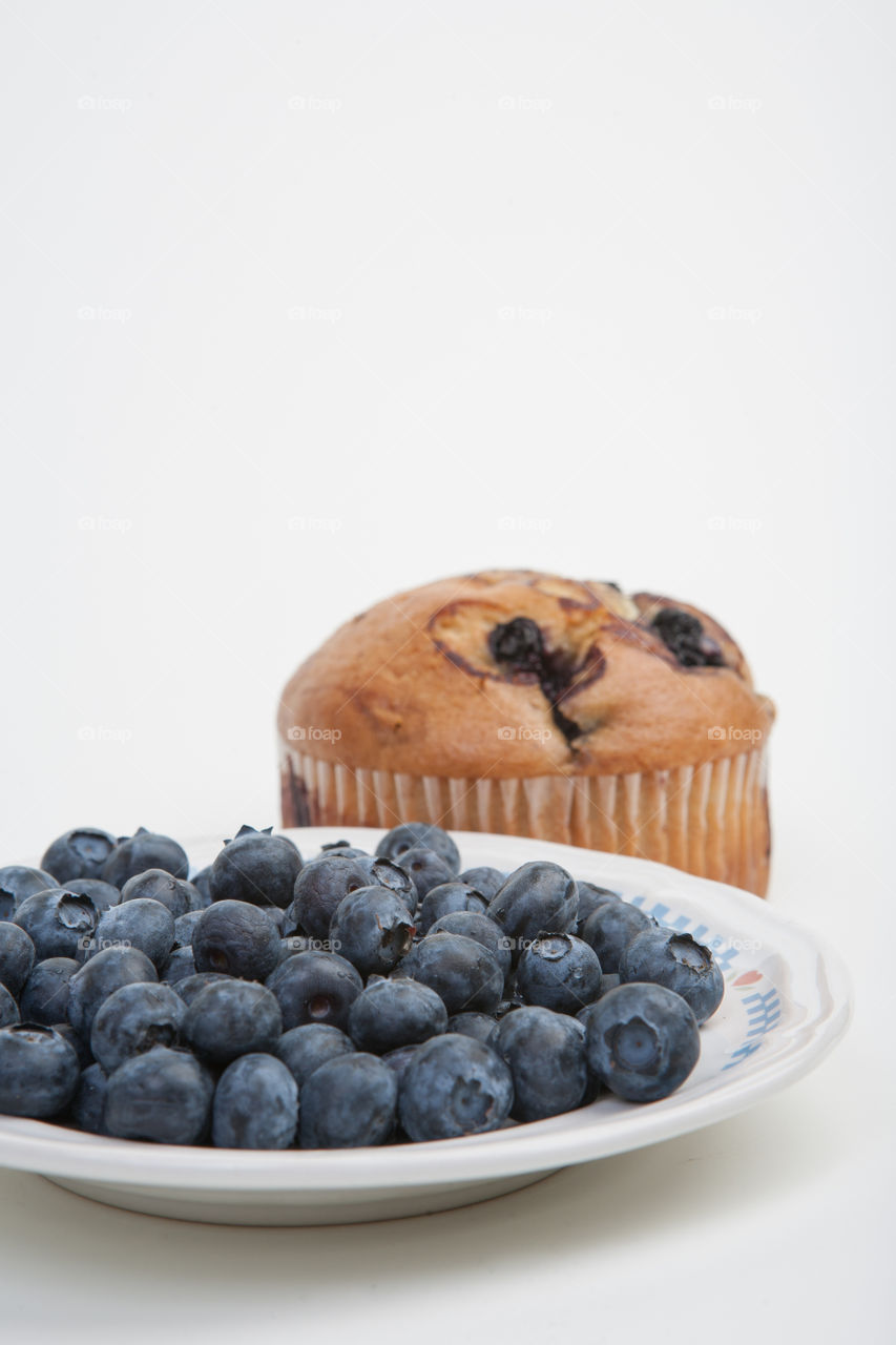 Vertical blueberry in bowl and muffin in background