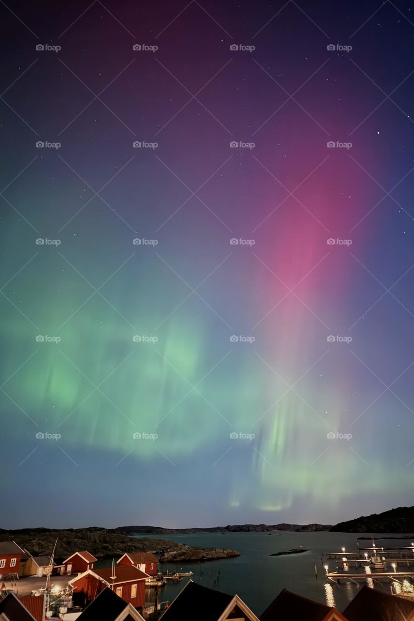 Colorful Northern lights in the sky above a small fishing village with red houses by the ocean in Sweden 