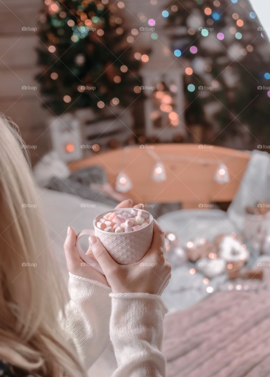 Cup with marshmallows in female hands on a background of Christmas decor