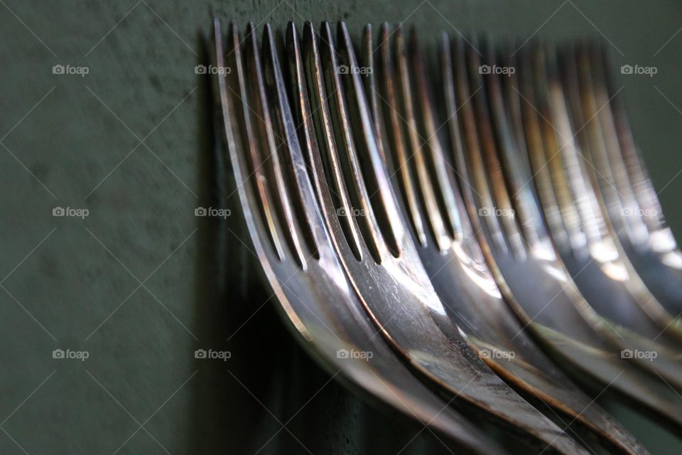 Close up of silver forks standing on green wall 