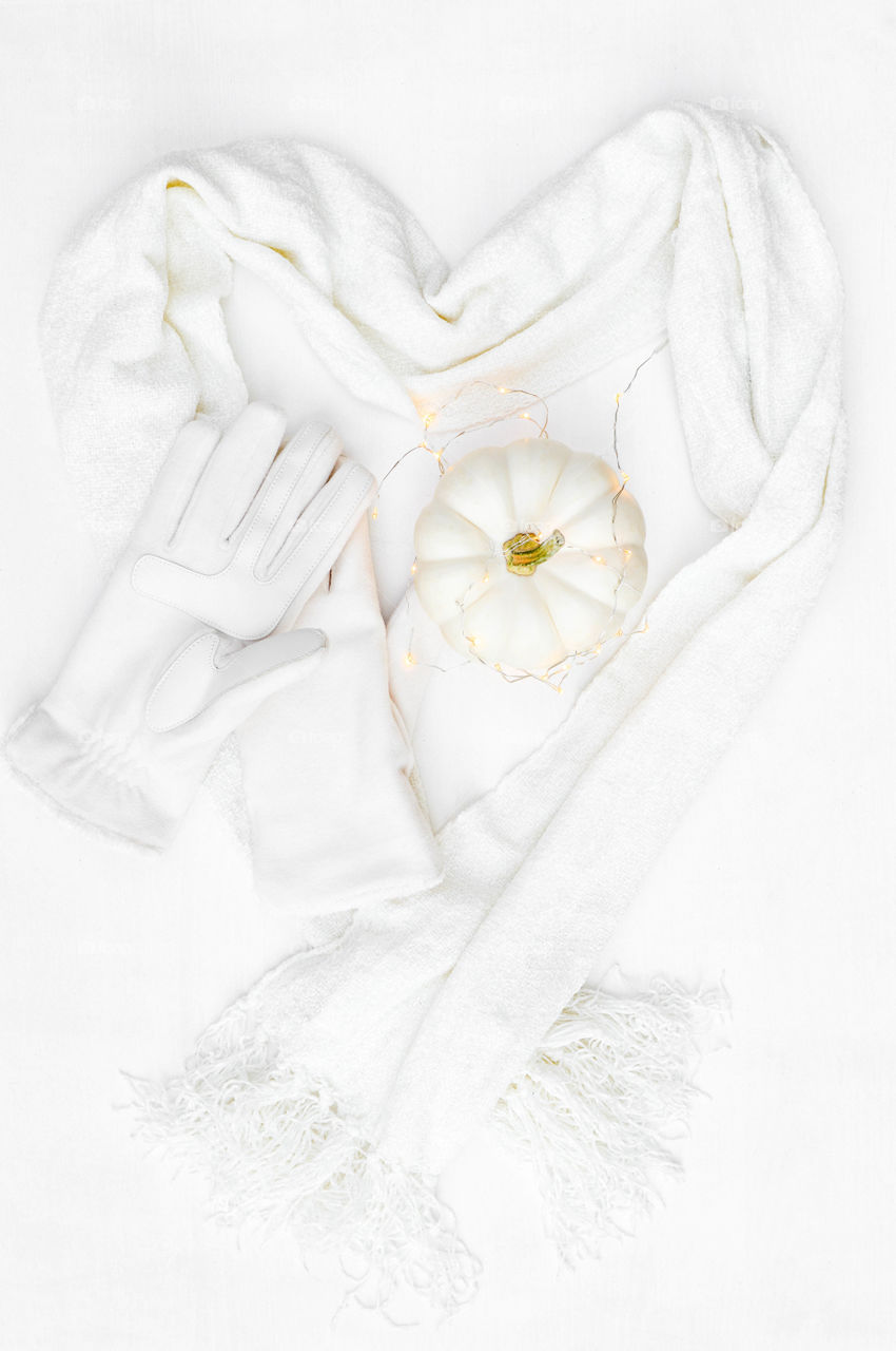 Monochromatic flat lay of a white scarf and gloves and white pumpkin against a white background