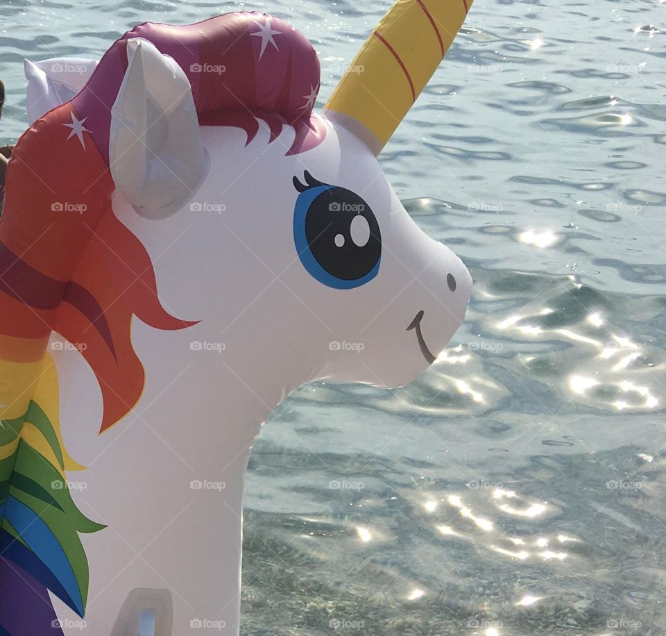 The joyful smile of a rainbow unicorn floaty against the backdrop of a sparkling blue sea in summer.