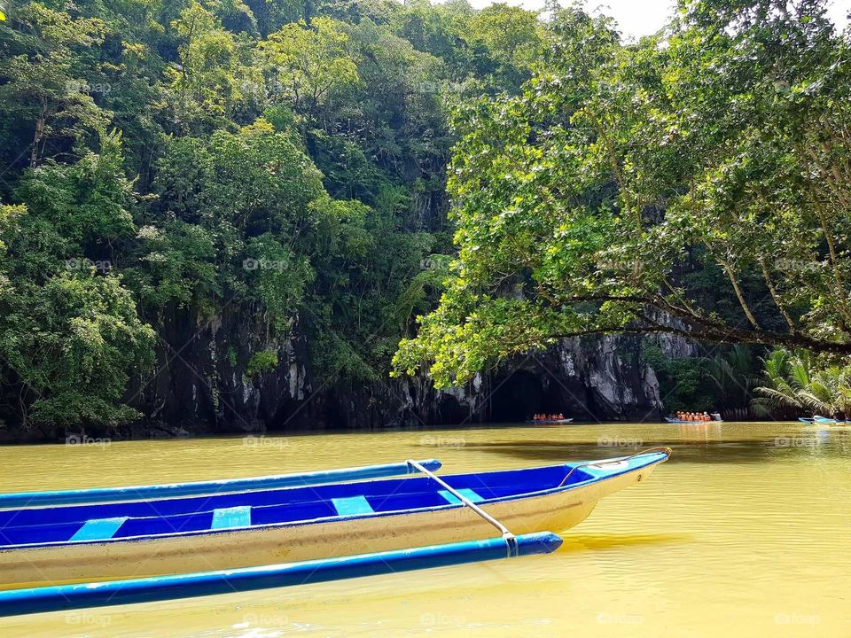 A relaxing view of an empty boat floating on the water with trees and cave on the background.
