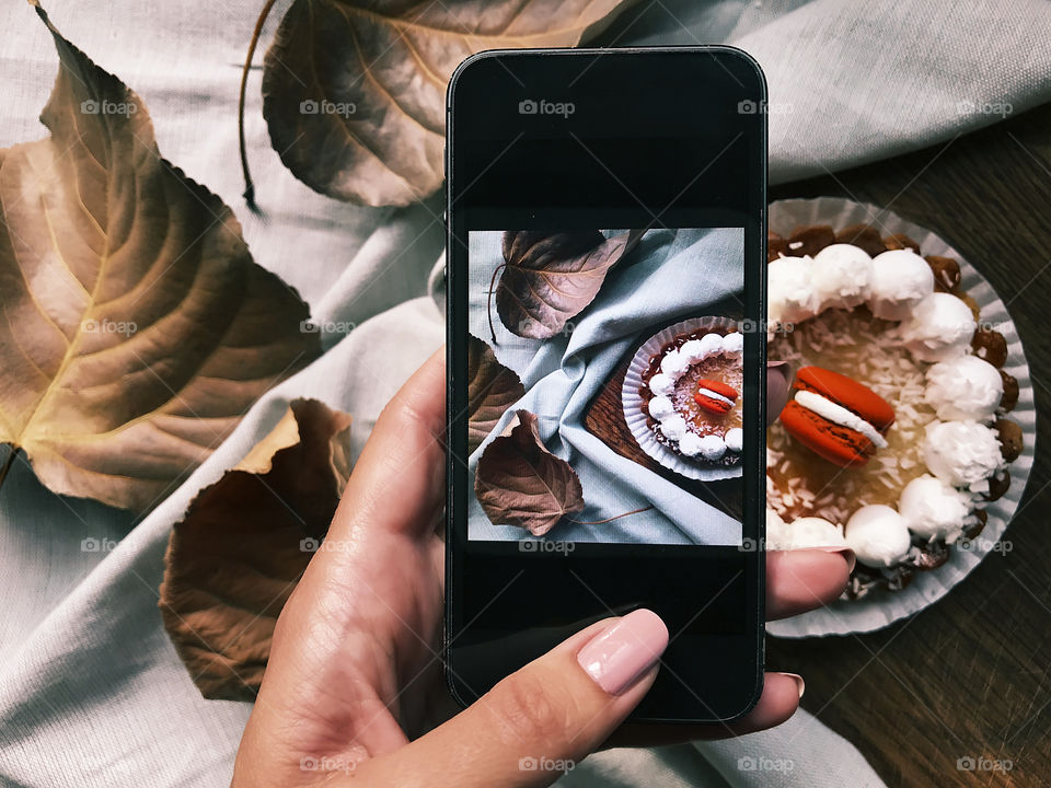 Female hand taking a photo of a yummy cupcake with orange macaroons using mobile phone 