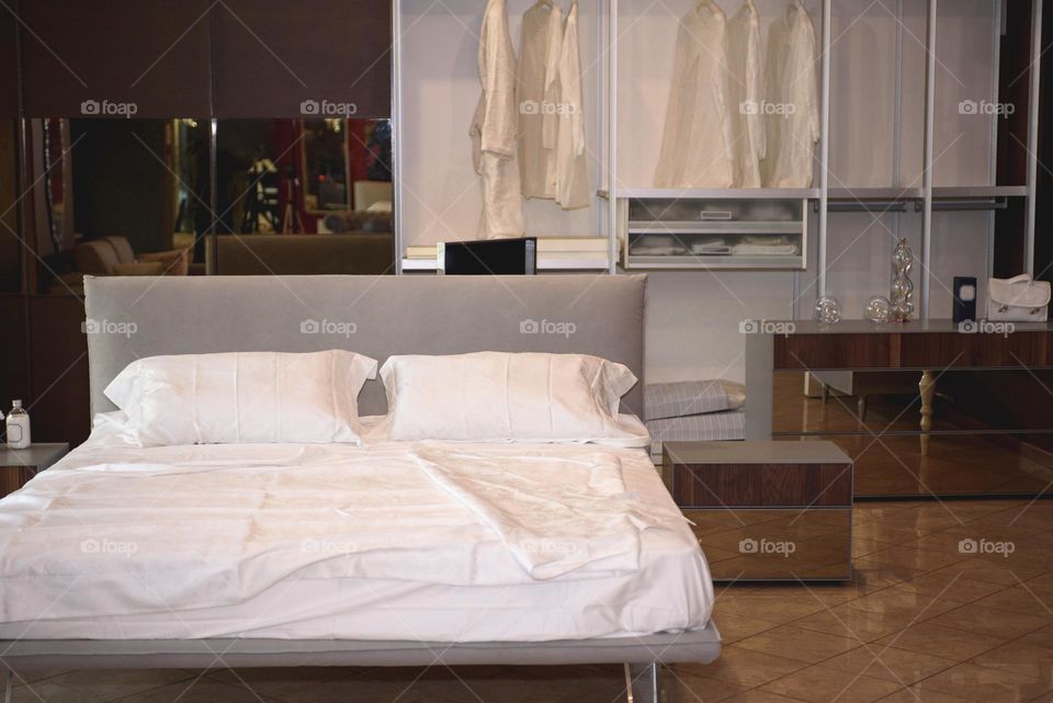 Modern bedroom in soft light colors. Large double bed and comfortable wardrobe with shelves.