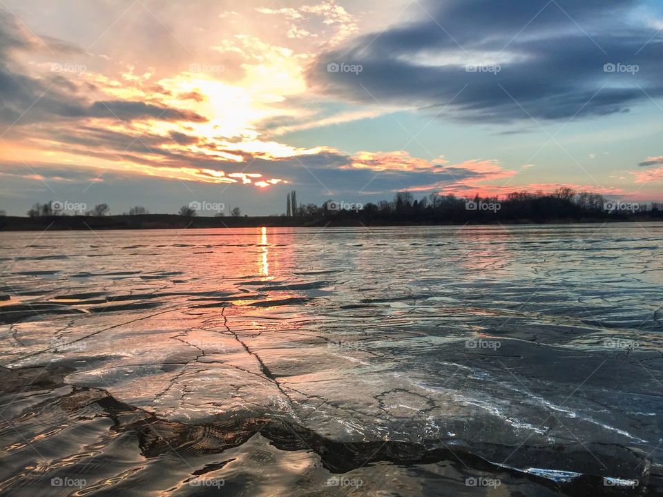 Frozen lake starting to defrost at sunset