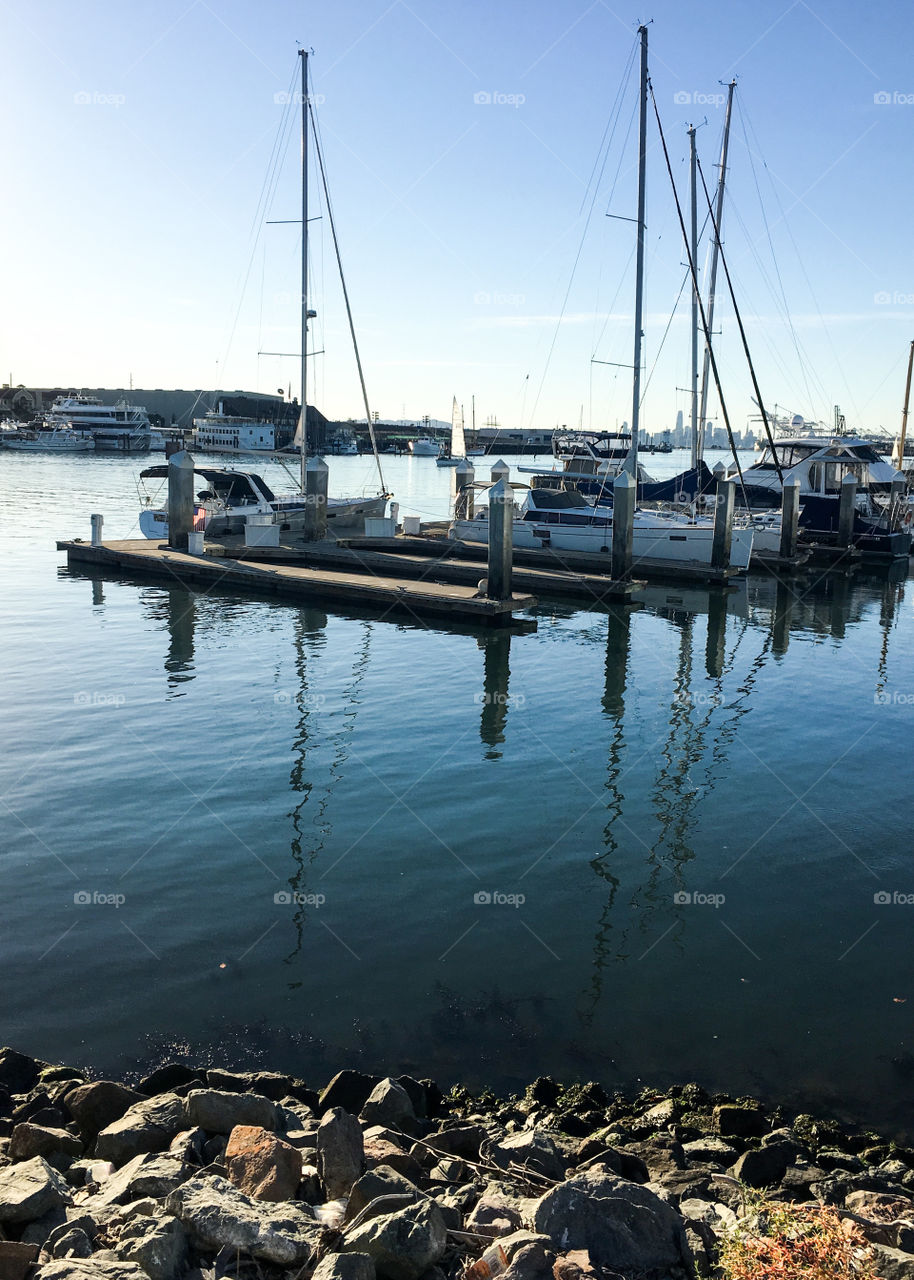 View of docked boats on a pier at a marina over blue waters and under blue skies.