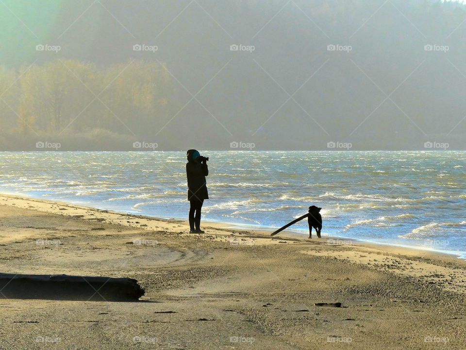 female photographer and dog with a stick at the beach