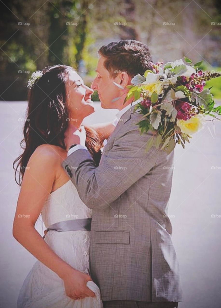 A beautiful young bride and groom lovingly embrace after wedding, sunshine illuminates their smiles