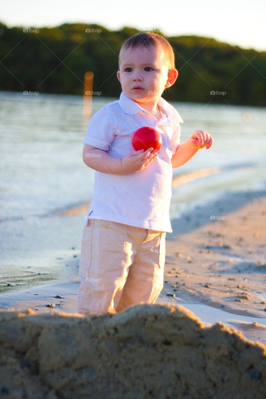 Boy standing on beach with holding red ball