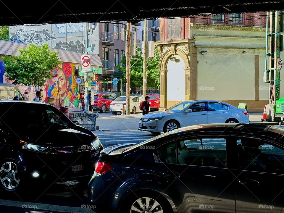 This is the “M” train overpass at “Myrtle Avenue” and “Broadway” in “Bushwick”, Brooklyn with bustling car traffic in the streets and the “La Lupe” art mural visible on the left on “Jefferson Street”. 2024. Hypnotic Productions