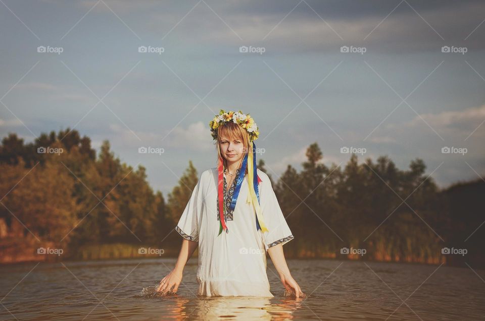 Happy Ukrainian girl,  woman in embroidery, wreath of flowers swimming in green lake in summer. Support Ukraine. Symbol