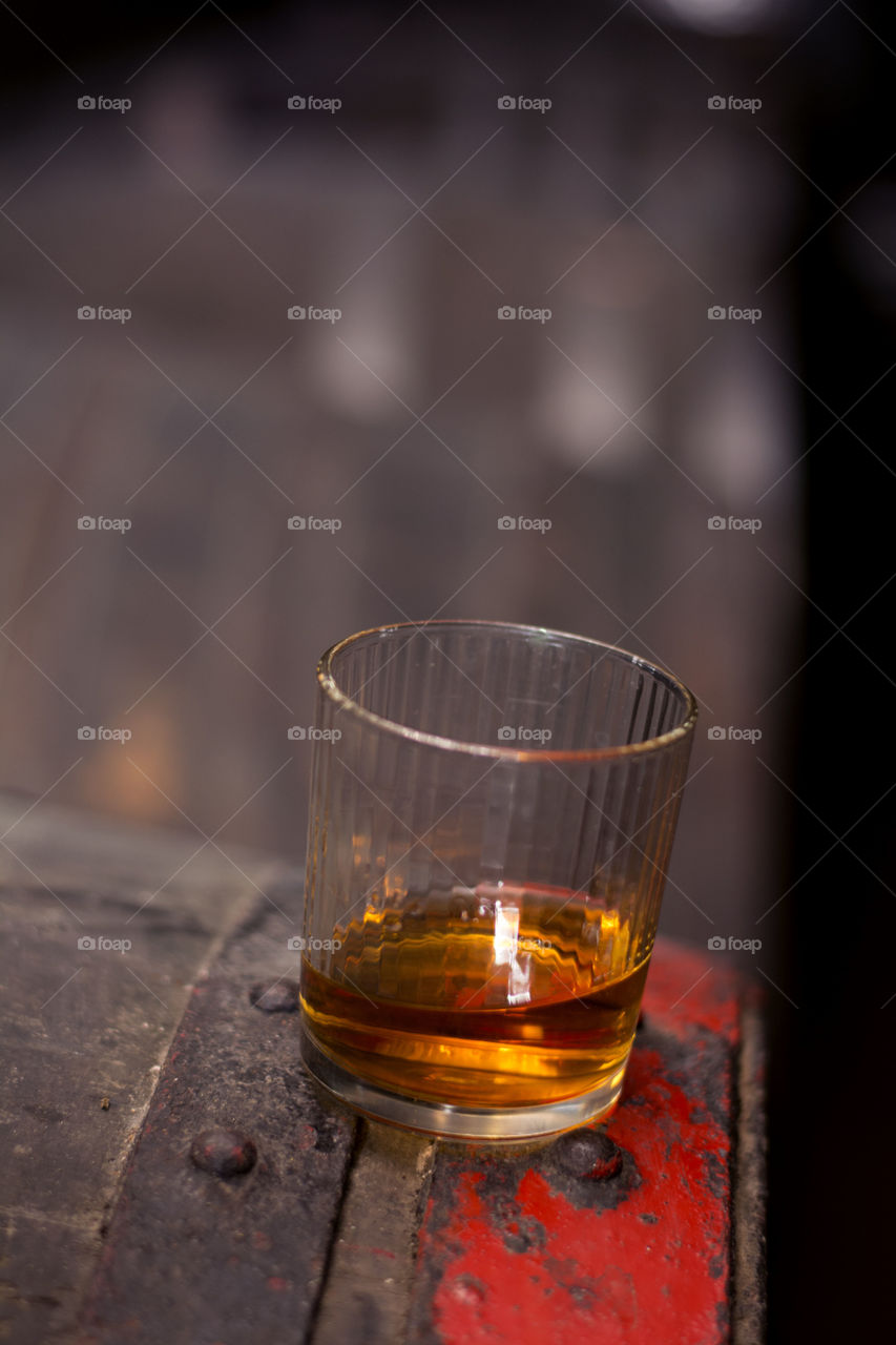 closeup of whiskey in glass. closeup shot of whiskey in glass on top of wooden barrel in distillery