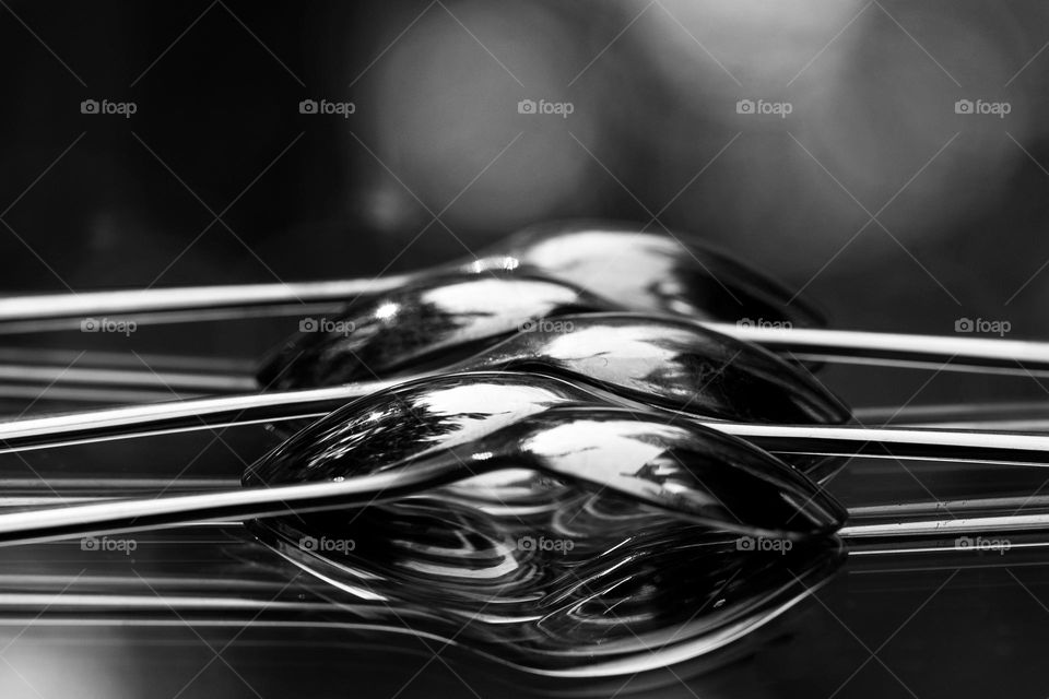 Black and white shot of overlapping spoons sitting on a mirror in the sunlight outside on my deck. Reflections provide depth and mystery to this optical illusion and natural light bokeh. 