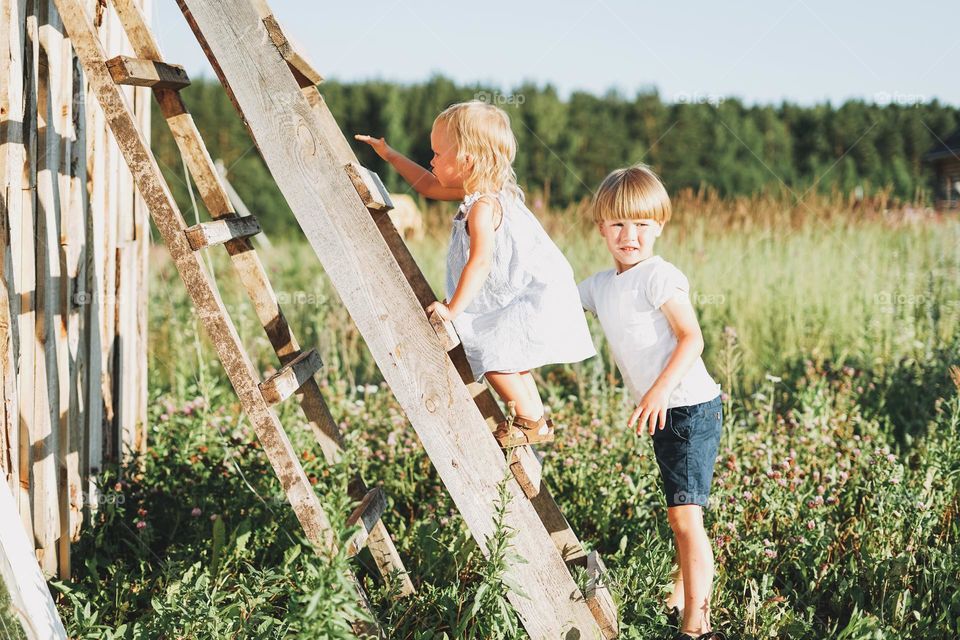 Cute siblings little girl and boy brother sister climbs up the ladder countryside cottagecor