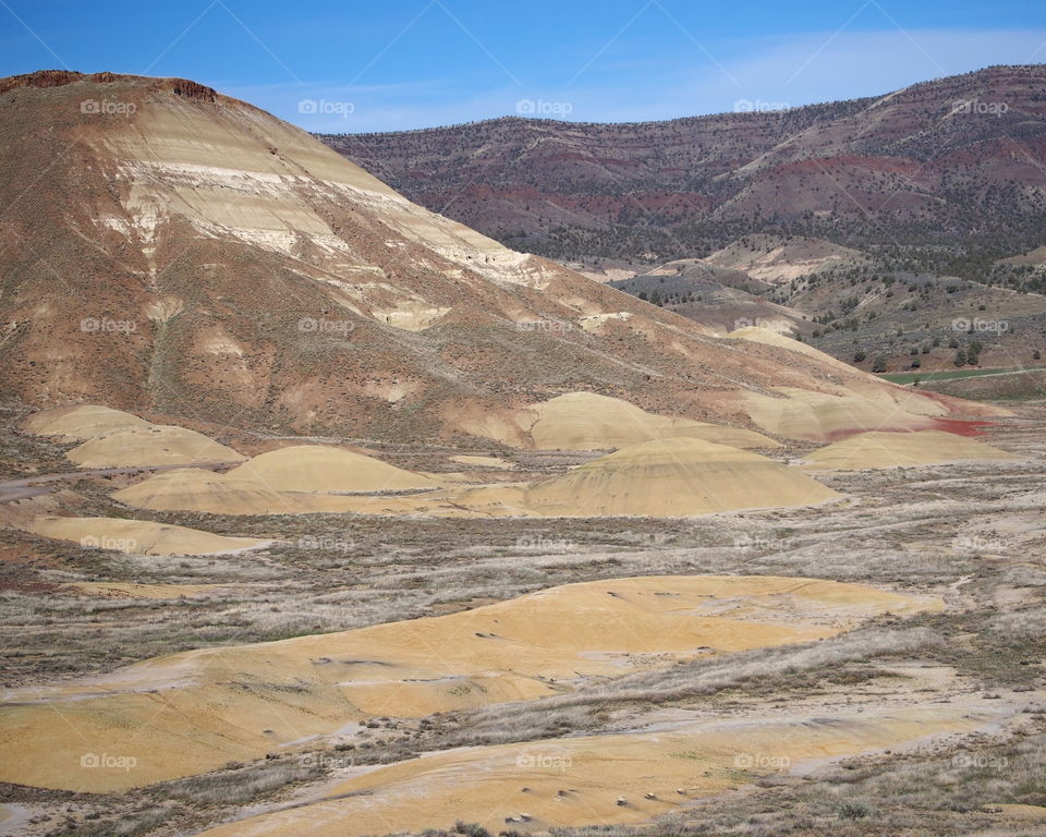 Sandy mounds at the base of brown, red, and black colored hills in the Painted Hills Unit of the John Day Fossil Beds National Monument in Eastern Oregon on a sunny day. 