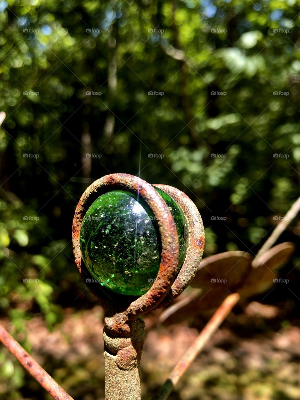 Sunlight on green glass marble in rusty metal garden ornament by woods 