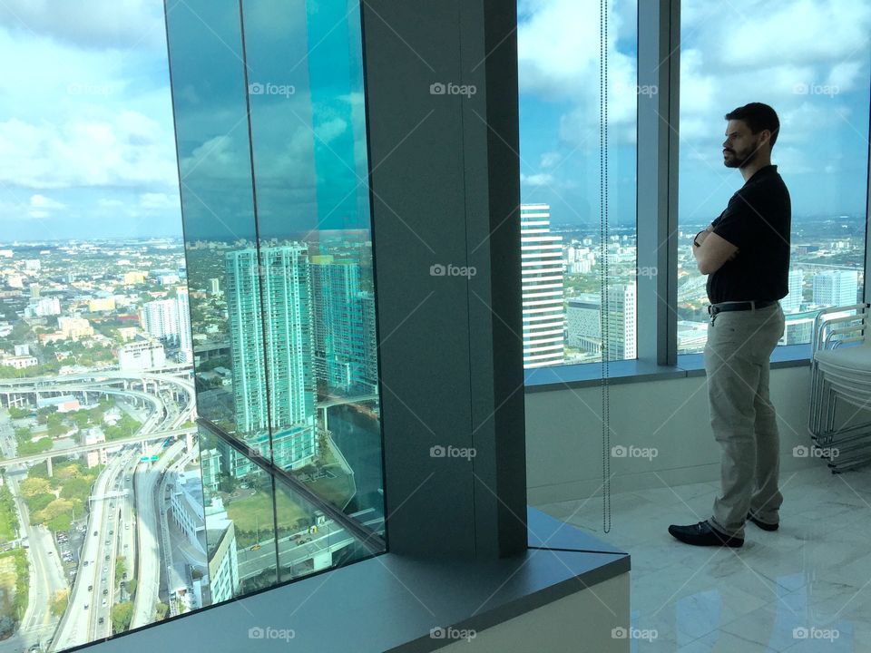 Contemplation. Young man standing by panoramic window looking outside