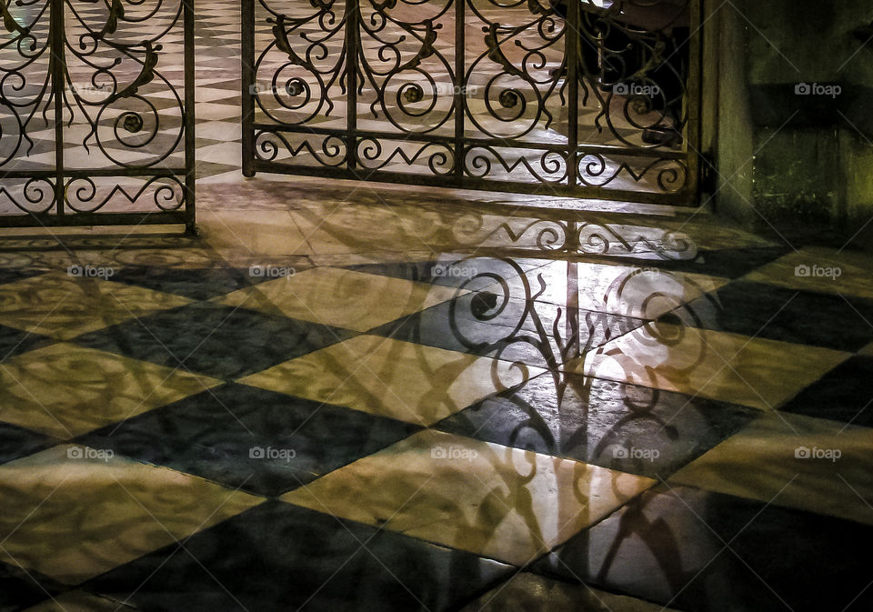 Shadow of caste iron gates on a checkered floor inside Notre Dame