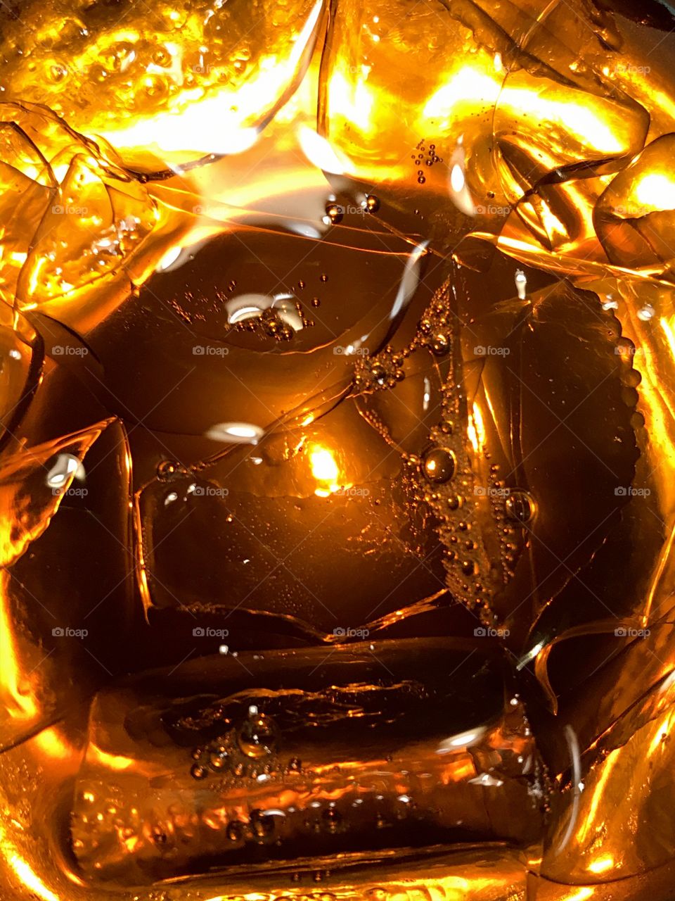 Artificial vs natural light: iPhone photo of a glass of iced tea. An overhead warm light and a iPhone flashlight light underneath the clear glass illuminate the amber tea & ice cubes giving it a golden hue that looks almost like flames. 