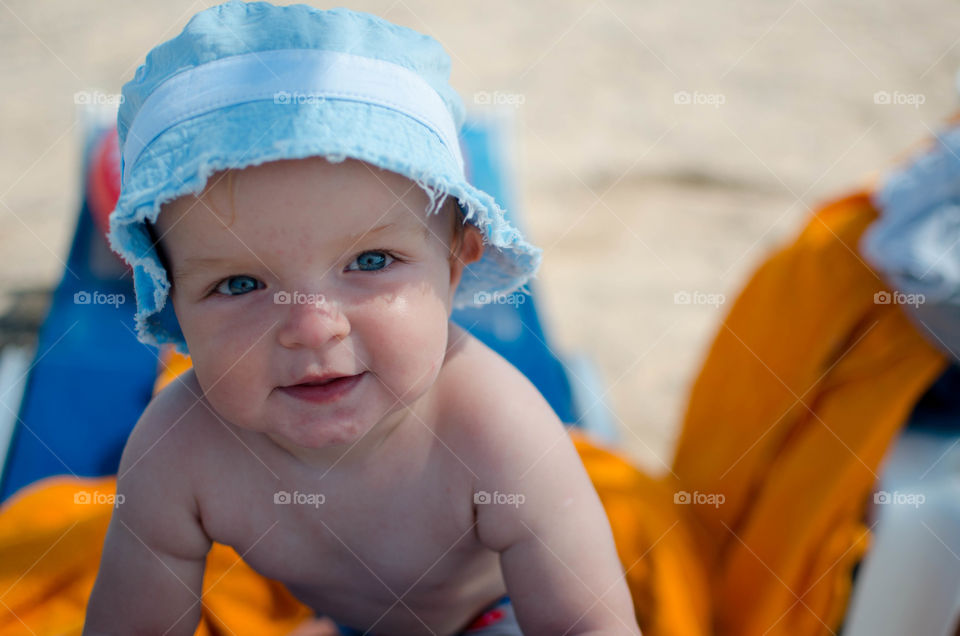 at a beach . baby in a blue hat