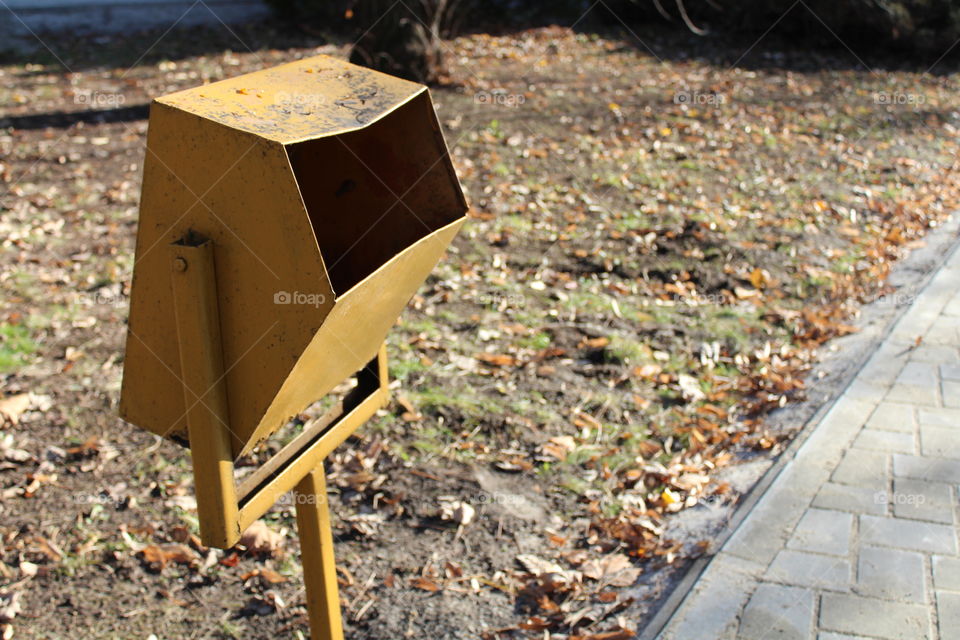 yellow public trashcan on the side of the stone path