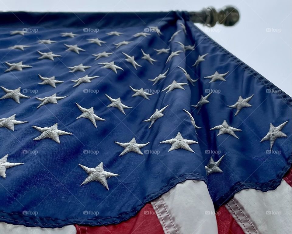 The American Flag hangs down from above, her bright colors of red, white and blue vibrant in the sun