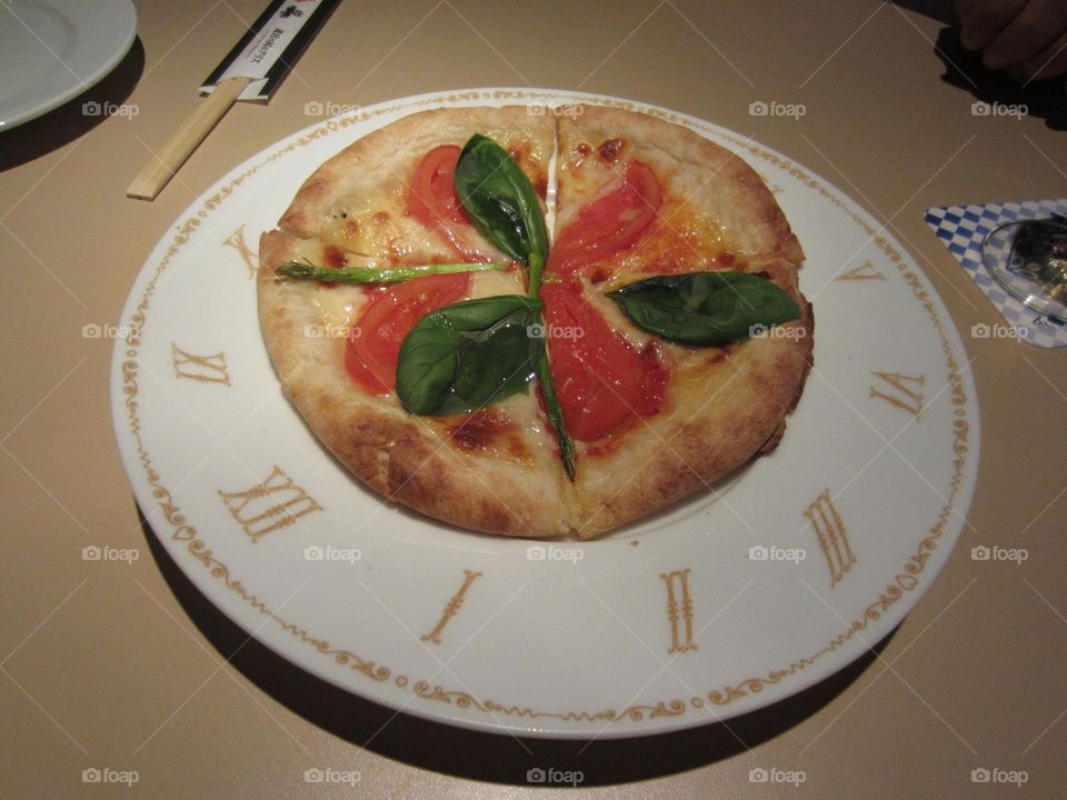 small Italian Margherita pizza on a plate that's like a clock with roman numerals