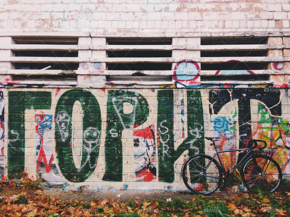 Grayish-black brakeless fixie bicycle standing in front of the wall decorated with bright colored wallart graffiti