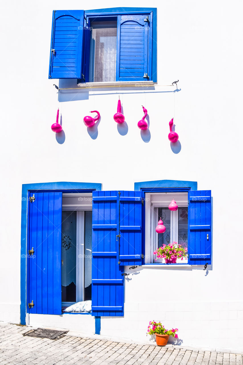 Greek Traditional House With Blue Windows , White Wall, Flowers And Pink Decorative Pumpkins
