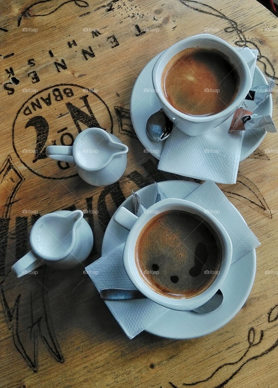 Two cups of coffee with milk jugs on wooden table