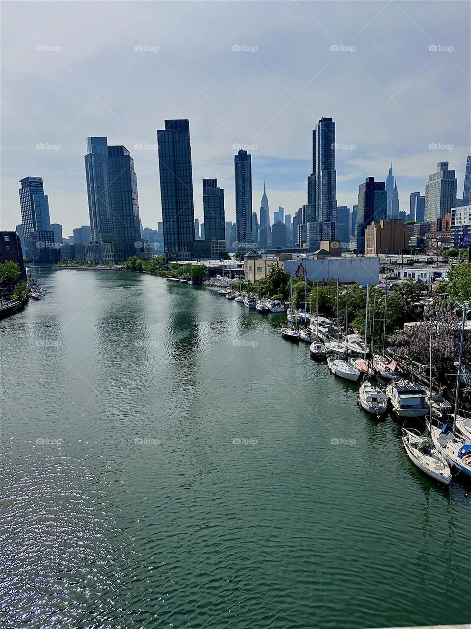 This is a panoramic view of “Newtown Creek” from the “Pulaski Bridge” that connects LIC, Queens to “Greenpoint”, Bklyn. Across the “East River” in the distance we see “Manhattan” including the “Empire State Building”. 2024. Hypnotic Productions
