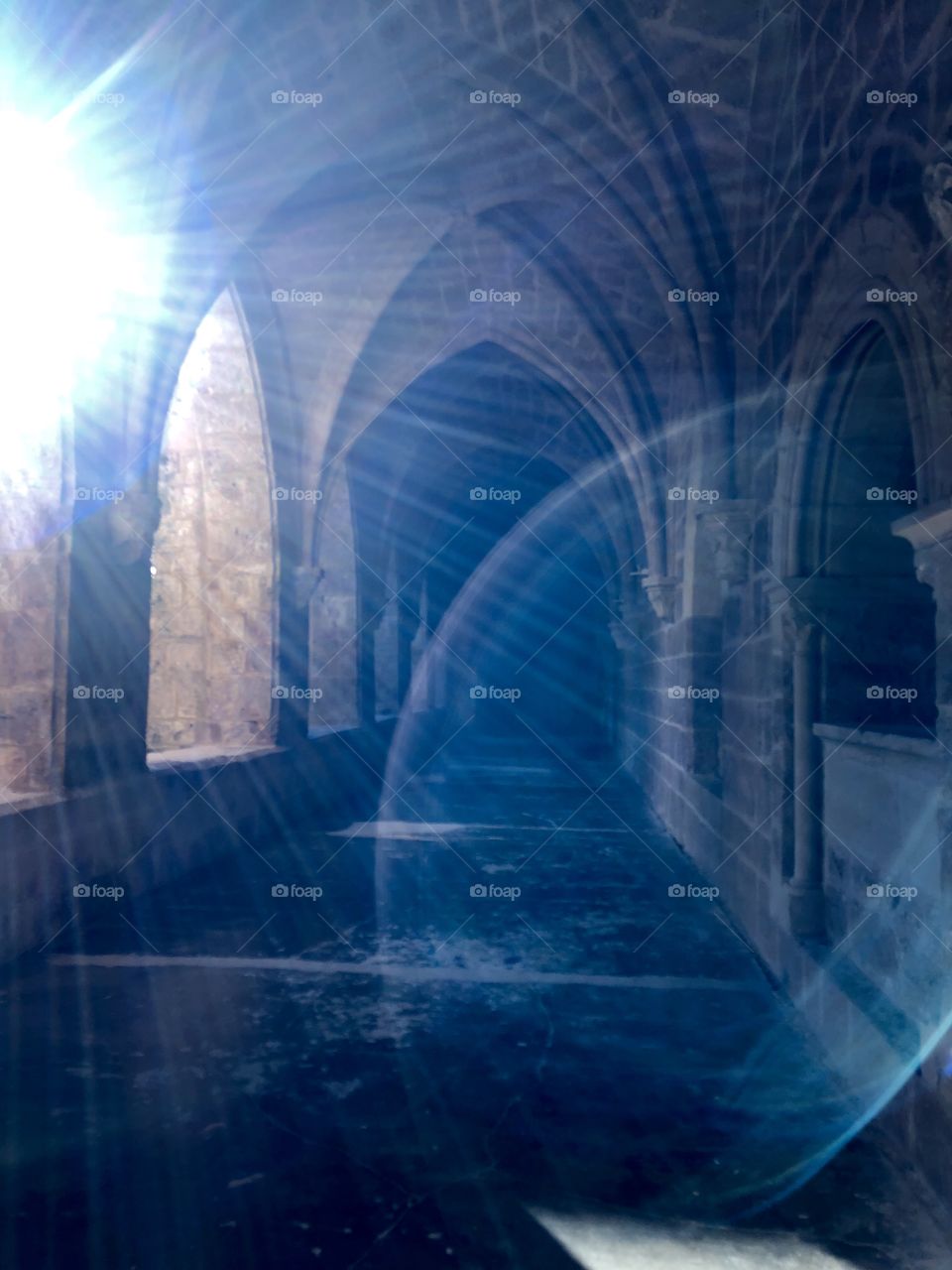 Multiple beautiful and haunting sun flairs shining down a dark hallway of a gothic monastery. 