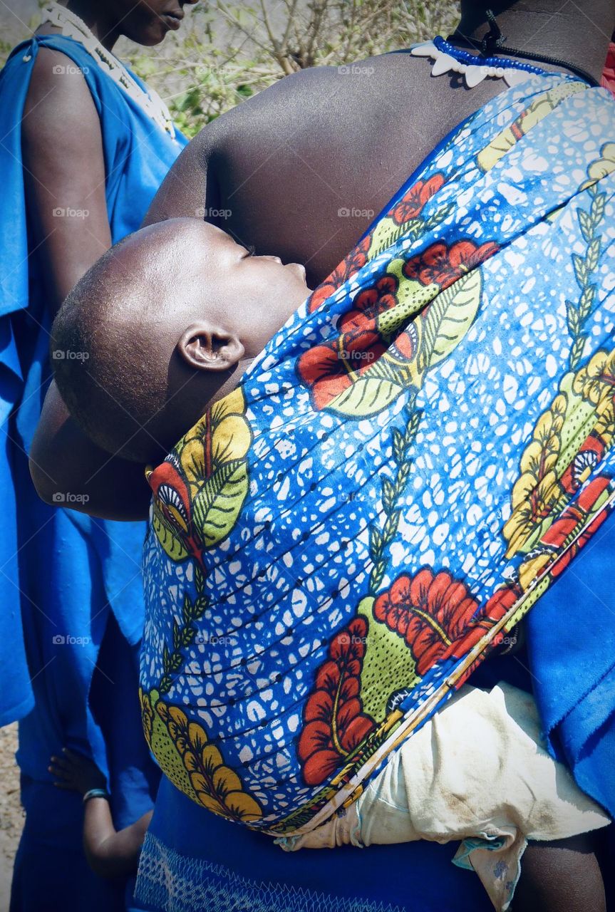 Loving mother carrying her sleeping baby on her back in a vibrant coloured sling 