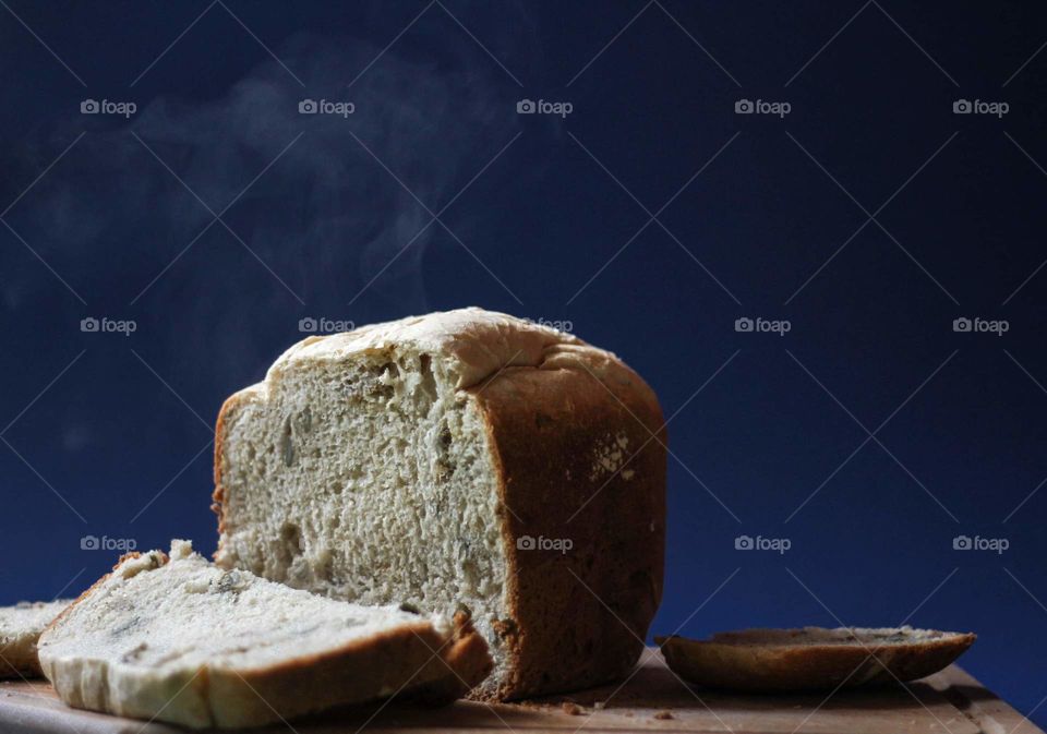 Hot loaf of bread and a slice of bread on the cutting board on dark hlue background