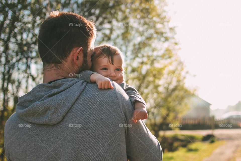 Cute baby boy on his dad's shoulders walking on village road outdoors, sensitivity to nature concept