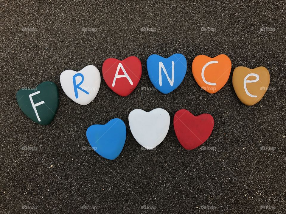 France, country name with colored heart stones over black volcanic sand
