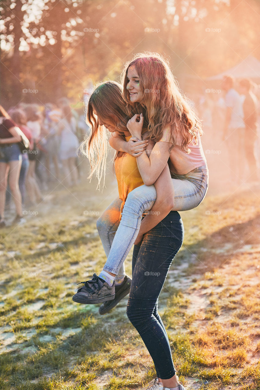 Portrait of happy smiling young girls with colorful paints on faces and clothes. Two friends spending time on holi color festival. Real people, authentic situations