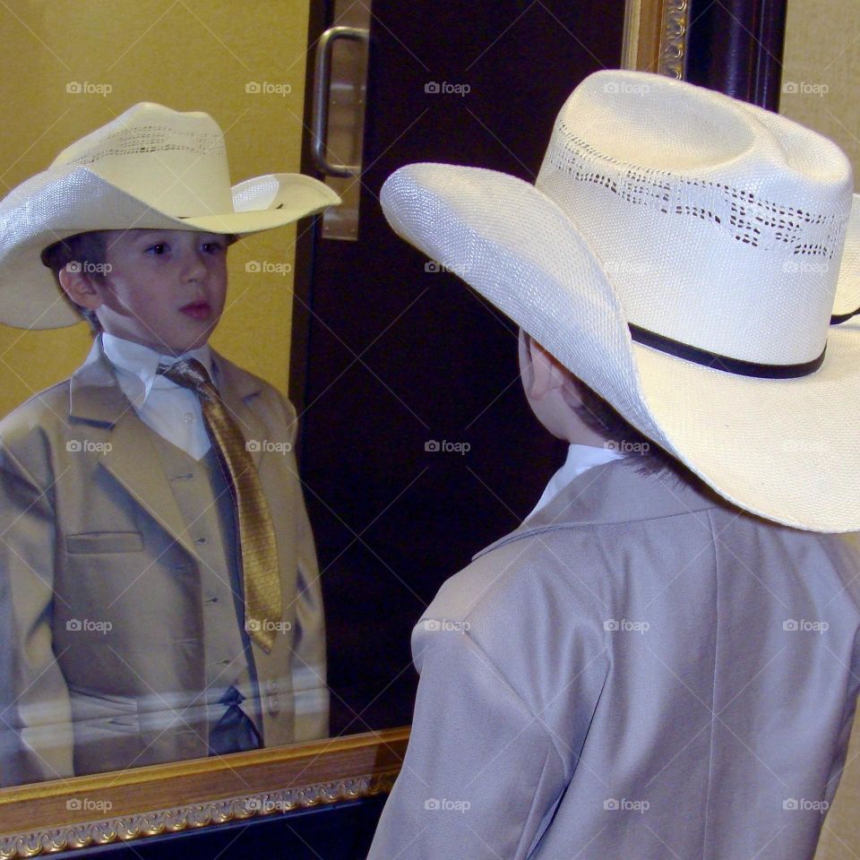 Young boy in a suit and cowboy hat looking at himself in a mirror