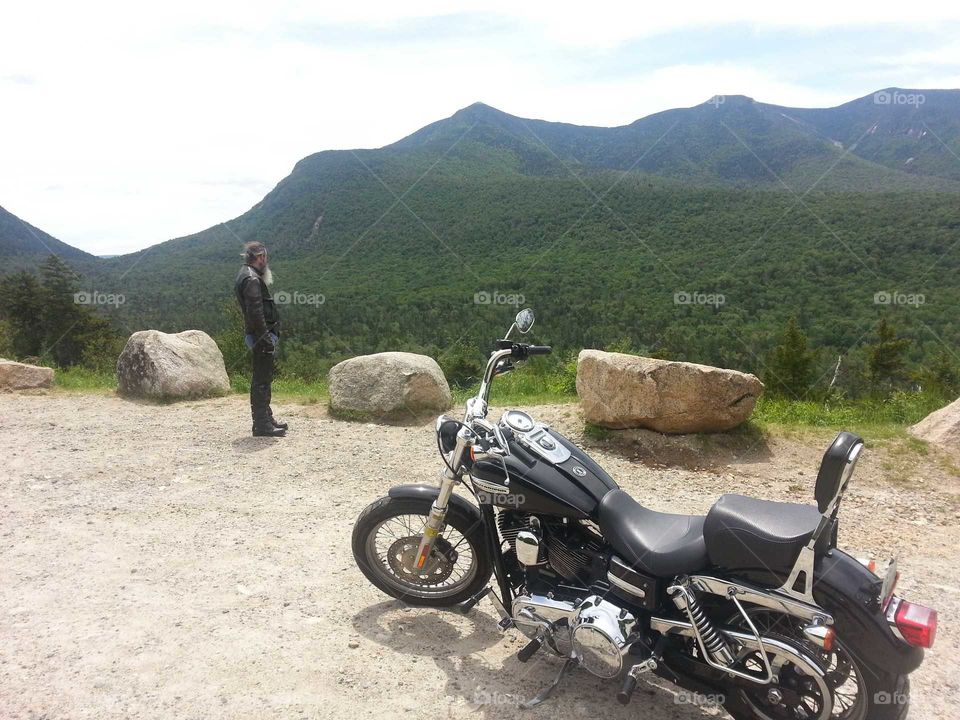 Man looks at mountain view with motorcycle in foreground