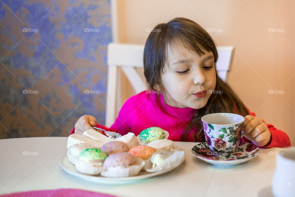 Little girl with cup of tea and cupcakes 