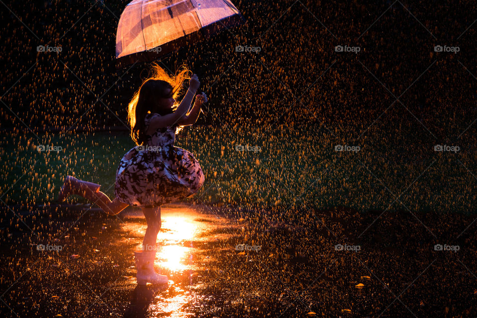 Stuck at home - so we're dancing in the rain! Image of my girl in the garden, playing with an umbrella in the rain with orange backlight.