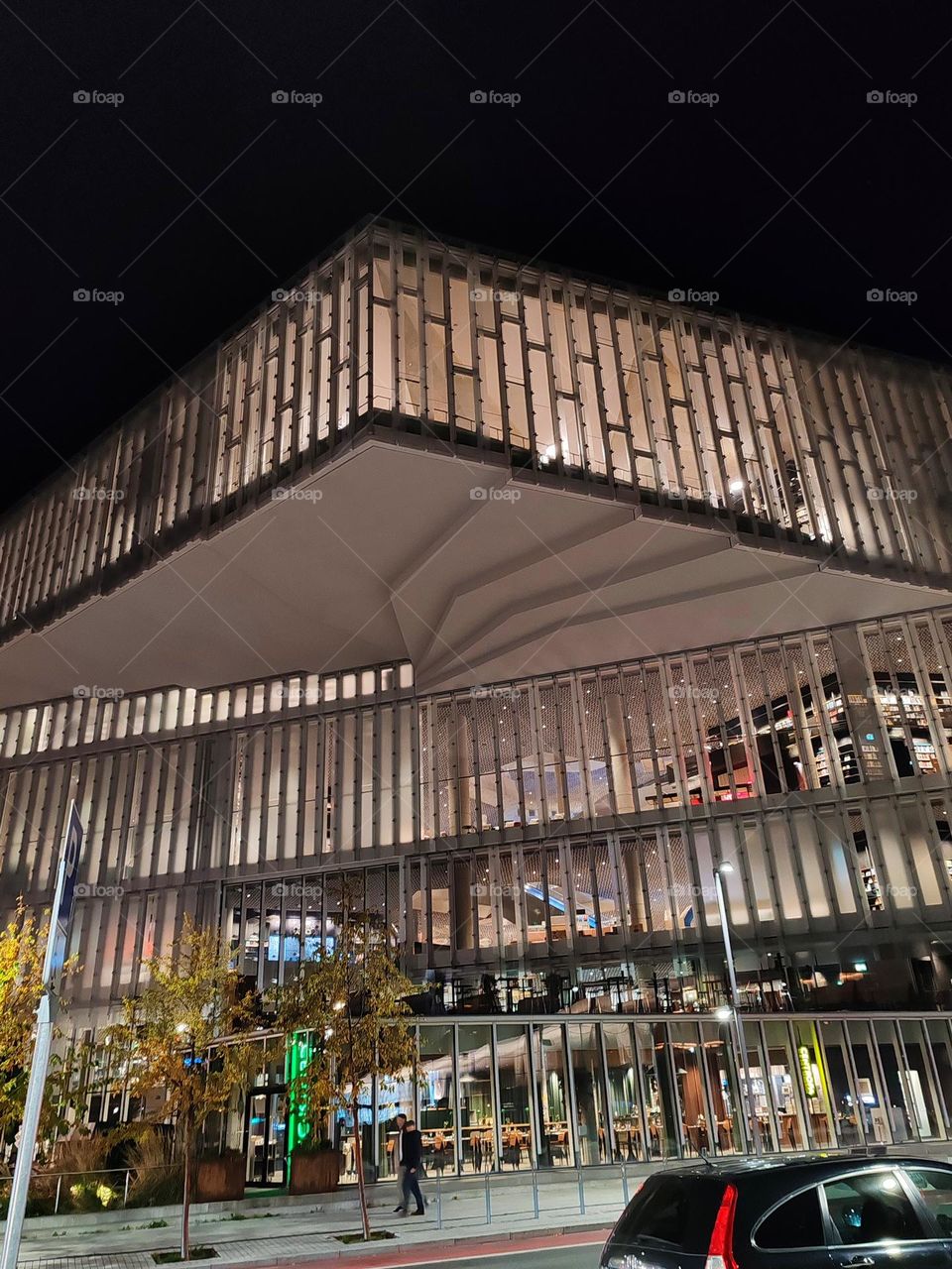 The image shows a modern architectural structure illuminated at night. The building features a distinct geometric design with a mix of sharp angles and smooth surfaces.