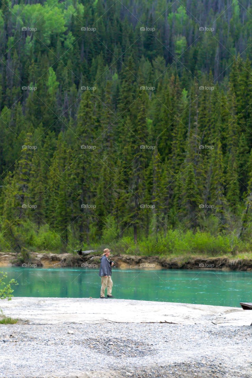 Male photographer walking by green river in Canada's Rocky Mountains 