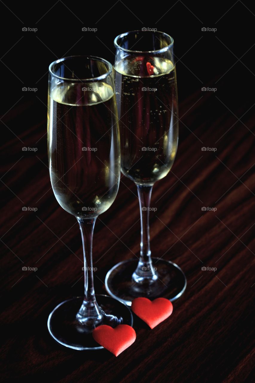 two glasses of champagne and two red hearts on a dark background in contrast