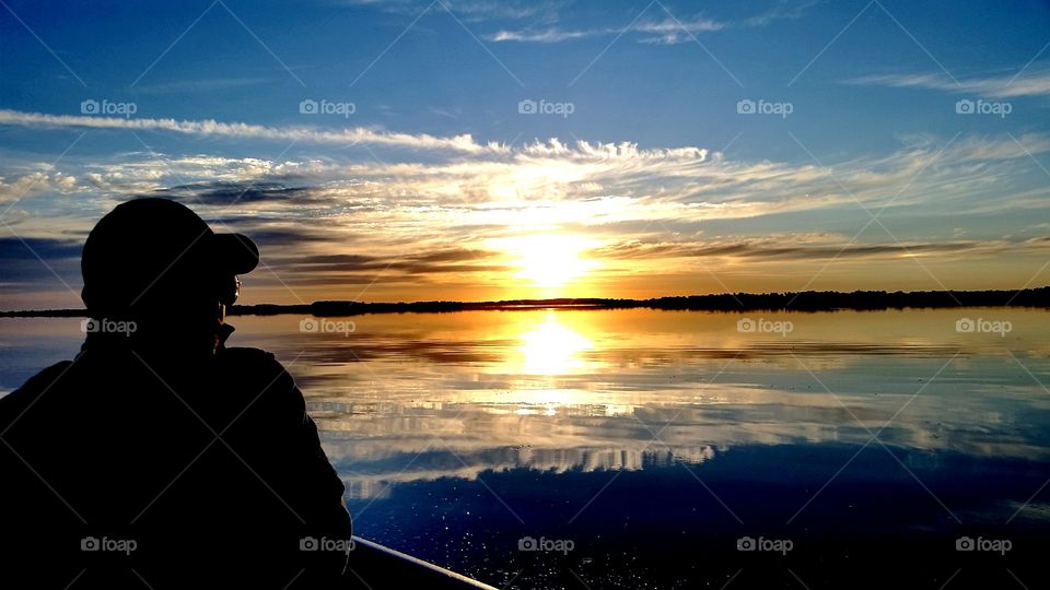 man in a boat, going fishing with a beautiful sunrise reflecting off the still morning water