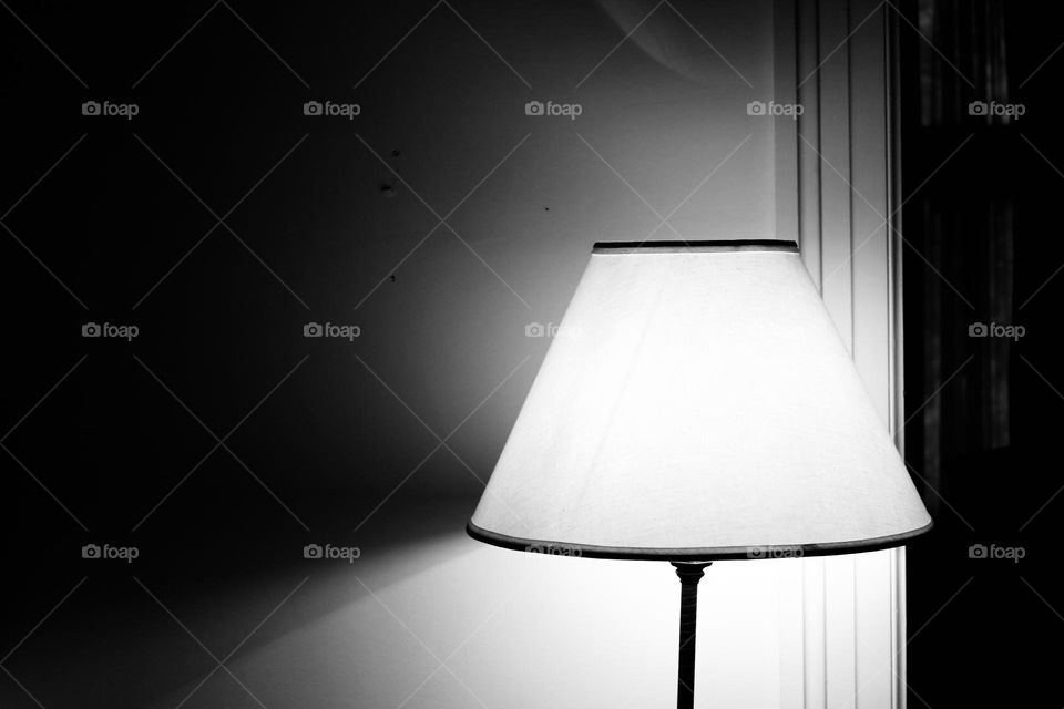 Floor lamp with shade illuminated shadows against white wall, black and white image, room for text, minimal