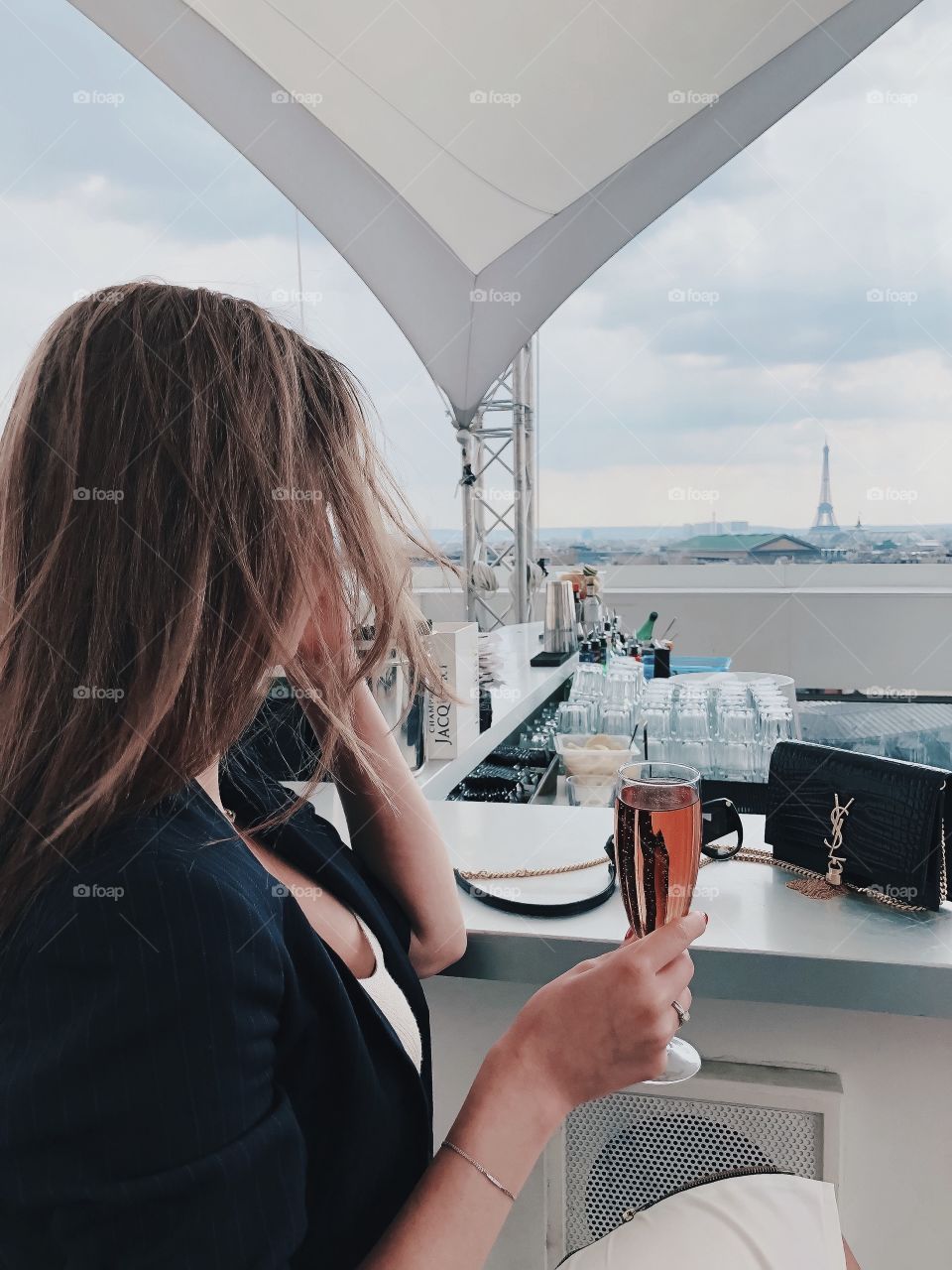 Woman with champagne in Paris. Luxury lifestyle. Glass of champagne. Brands bag. French style. Travel girl. Roof. Tour Eiffel. 